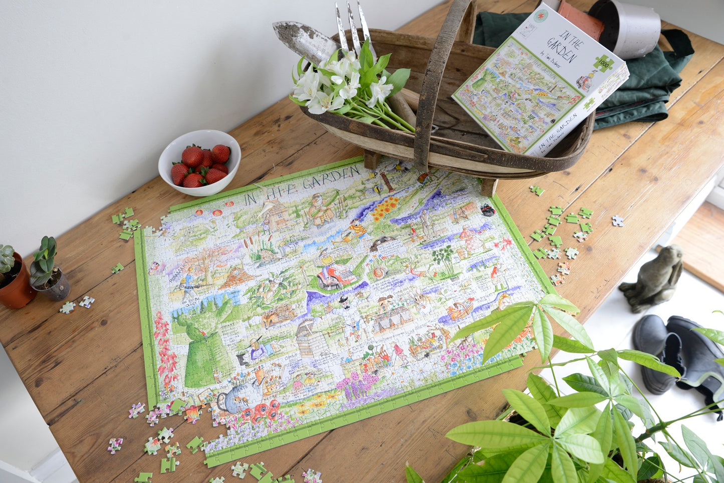 Jigsaw puzzle on a wooden table with a book and small bowl of strawberries.